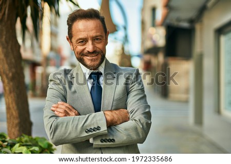 Middle age businessman with arms crossed smiling happy at the city.