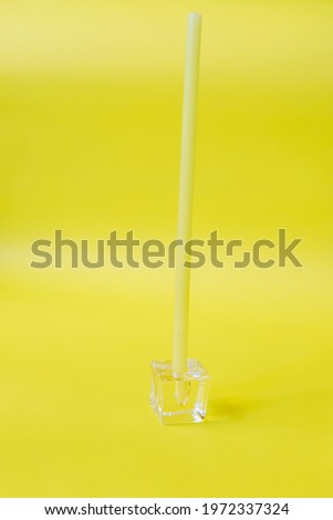 Long slim and elegant candles and transparent glass candle holder on yellow background
