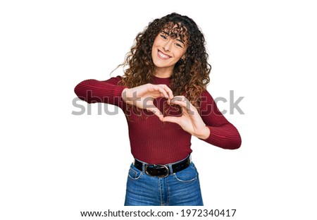 Young hispanic girl wearing casual clothes smiling in love doing heart symbol shape with hands. romantic concept. 