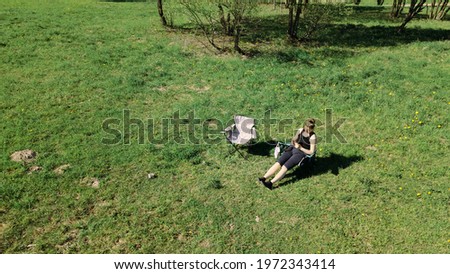 Woman in a camping chair on a meadow in a spring park. There are young foliage and white flowers on the trees. Aerial photography of nature.