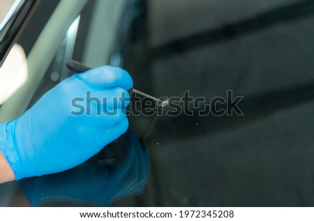 Mechanic is expanding a stone chip in a car windscreen before repairing Royalty-Free Stock Photo #1972345208