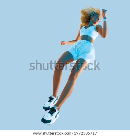 Profile picture of inspired energetic caucasian female in sportswear running and jumping, isolated along gray background. Motivation fitness concept studio photo. Creative blue light