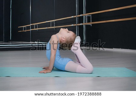 little girl does gymnastic exercises on a sports mat in the classroom of a choreographic school.