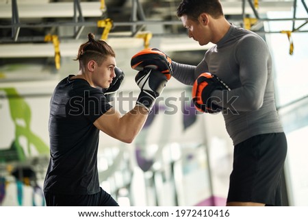 Young athletic man having boxing training with his instructor at health club. Royalty-Free Stock Photo #1972410416