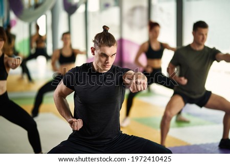 Male martial artist in fighting stance exercises punch during sports training at health club. Royalty-Free Stock Photo #1972410425