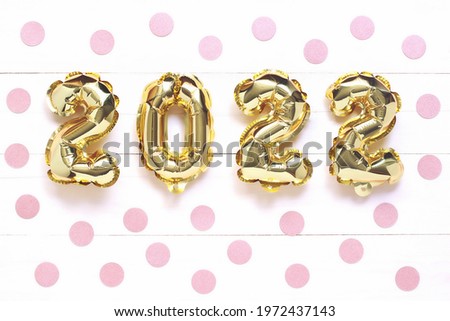 Christmas or New Year background. 2022, made of golden balls, on a white wooden background, with pink confetti. Postcard or calendar. Happy New Year or Merry Christmas.