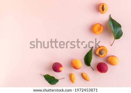 Flat lay of ripe red apricots sliced in halves and quarters with green leaves on the pink background Royalty-Free Stock Photo #1972453871