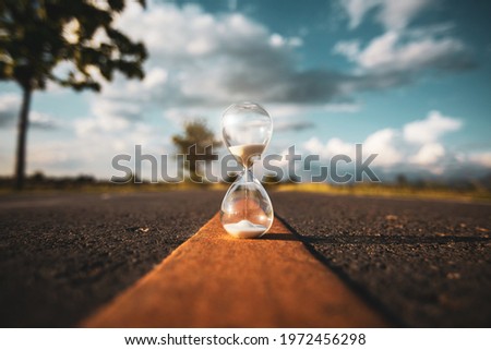 Hourglass on open road at sunset time. Life time passing concept.  concept time is money. Royalty-Free Stock Photo #1972456298