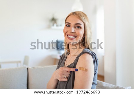 Woman pointing at her arm with a bandage after receiving COVID-19 vaccine. Young woman showing her shoulder after getting coronavirus vaccine at vaccination center.