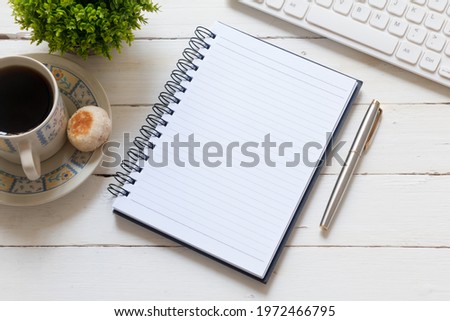 Note pad, pen, keyboard and coffee on white wooden desk