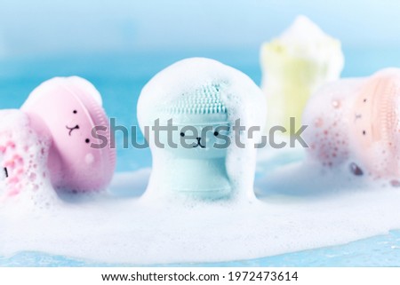 Silicone massage brushes for washing with funny faces in water covered with foam. Cleanliness and freshness, personal care concept Royalty-Free Stock Photo #1972473614