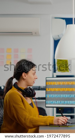 Photo editor specialist working on computer in creative office environment using stylus pencil. Retoucher woman retouching fashion assets with model in digital graphics editing software, color grading