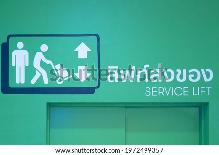 Green service elevator with working human and arrow sign is in department store or office in urban area.