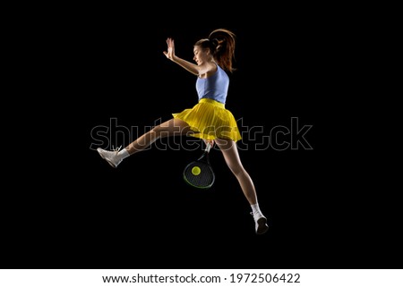 Flying. Young sportive caucasian woman playing tennis isolated on black studio background, action and motion concept. Fit professional sportswoman training, practicing. Copyspace for ad.