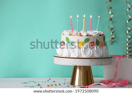 Delicious birthday cake and party decor on white wooden table against turquoise background, space for text