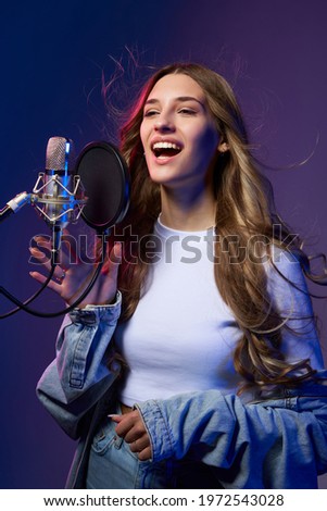 Girl blogger recording audio or singer. Happy smiling girl with microphone, studio shot with dual light