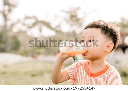 Portrait of little boy drinking orange juice in a glass with bike. Natural background.