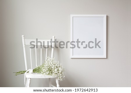 16x20 thin white vertical frame mockup template, hanging on a neutral coloured wall. Fresh bunch of flowers flowers sitting on an old, white, rustic chair.