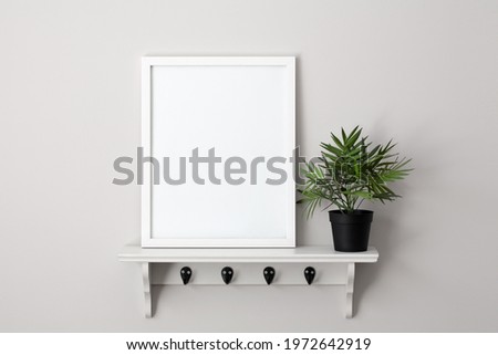 11x14 white vertical frame mockup template sitting on a white shelf next to a small green plant.