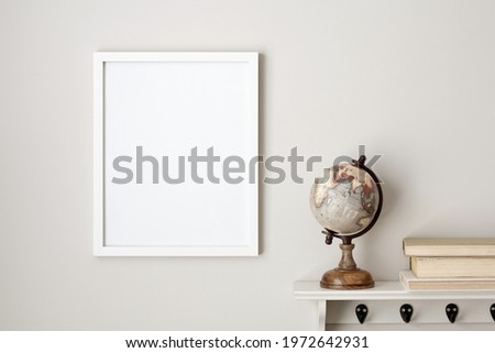 11x14 thin white vertical frame mockup hanging on a neutral coloured wall, next to a white shelf with a desktop globe and a stack of vintage books. Template for travel art or quotes.