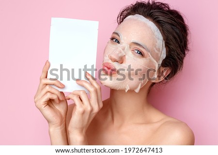 Smiling woman holds cosmetic packaging of facial mask and send air kiss. Photo of attractive woman with perfect skin on pink background. Beauty and Skin care concept
