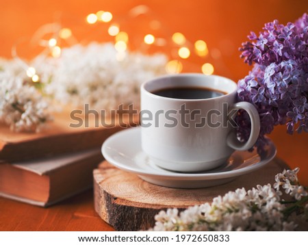 A white cup of coffee on a wooden table. Blooming branches of white lilac, old books