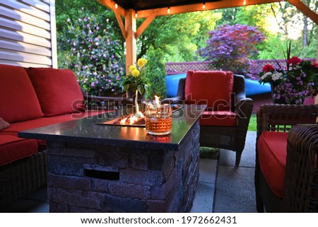Outdoor patio set with a gas fireplace a glass of scotch whiskey on ice and potted flowers under a gazebo Royalty-Free Stock Photo #1972662431