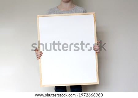 Child holding a large, thin wooden frame mockup template. Vertical orientation.