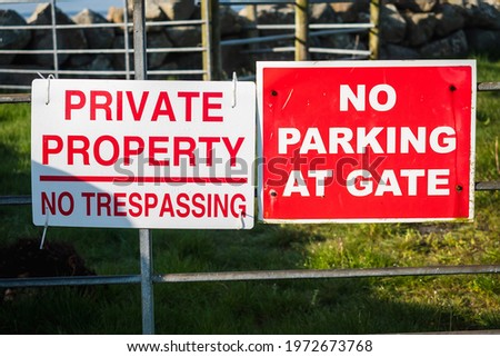 Private property no trespassing and no parking at gate signs on a metal gate. Entrance to a agriculture land. Stone fence in the background