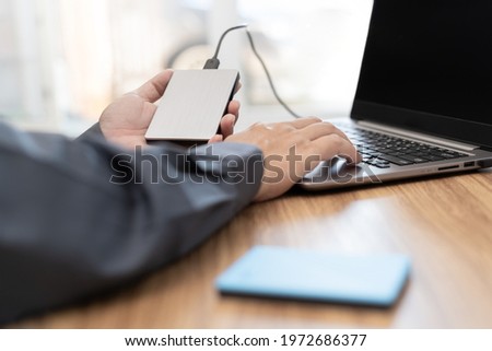 External backup disk in hard a man connected to laptop computer safety personal data copy Prevent data corruption in the computer system Royalty-Free Stock Photo #1972686377