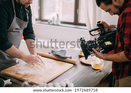 Director of photography with a camera in his hands on the set. Professional videographer at work on filming a movie, commercial or TV series. Filming process indoors, studio Royalty-Free Stock Photo #1972689758