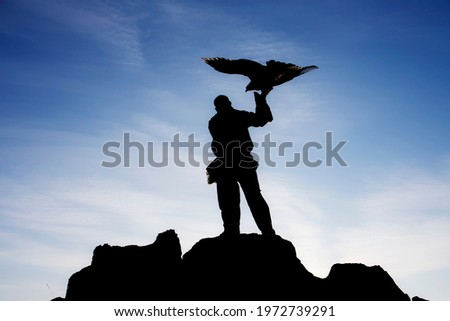 Mongolian man standing holding an eagle on a high mountain, silhouette image