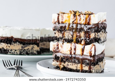 Stacked pieces of creamy chocolate, vanilla and mocha layered ice cream pie with the full pie in behind. Royalty-Free Stock Photo #1972743350