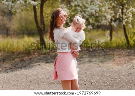 happy young mother and two-year-old girl whirling. people in white clothes spring