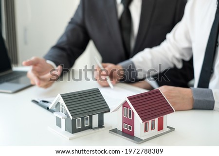 A real estate agent with a House model is talking to clients about buying home insurance. Real estate Home insurance concept.