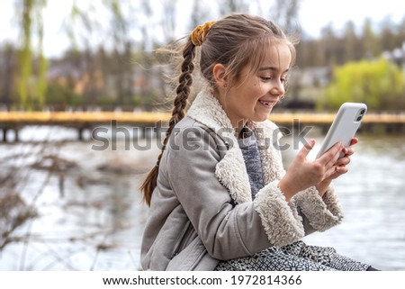 Close-up of a little girl with a phone in her hands on the background of nature.
