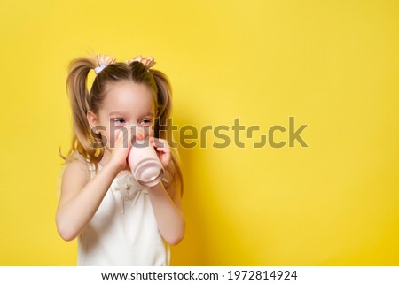Little girl drinks yogurt from a glass isolated on yellow backdround. Healthy eating concept. Banner with copy space.
