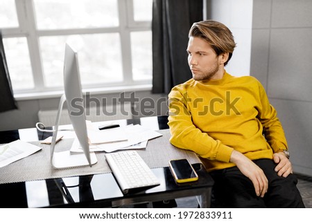 Pensive male freelancer working on new project, sitting at the desk in home office. Handsome young businessman or student lost in thoughts, developing new company strategy, remotely work concept