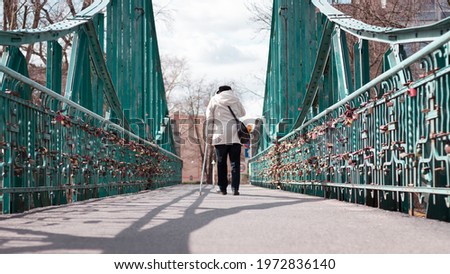 Elderly woman with a cane in her hand crossing the green bridge in the city