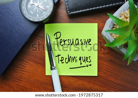 Selective focus of compass, pen, flower and sticky note written with PERSUASIVE TECHNIQUES.  Royalty-Free Stock Photo #1972875317