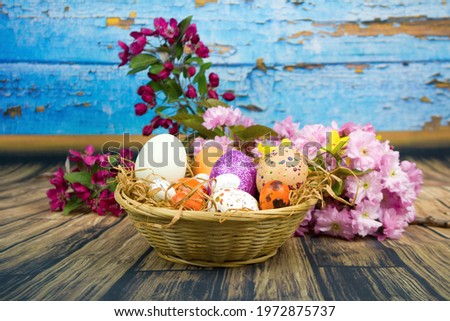 Color eggs decorated with wax and glitter in a basket and branches of ornamental cherries.