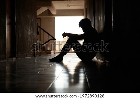 Silhouette of lonely young man wearing surgical mask feeling depressed and stressed sitting in the dark walkway, lonely and unhappy concept. Royalty-Free Stock Photo #1972890128