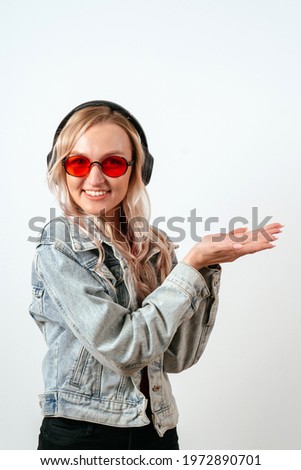 Portrait of a blonde woman in headphones on a white background, holds a hand, advertising, promo, copyspace, recommend, propose, choose.