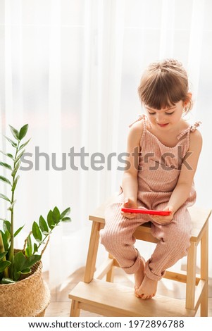 Little girl with mobile phone sitting alone. She is watching cartoons on smartphone. Digital generation and phone addiction concept.