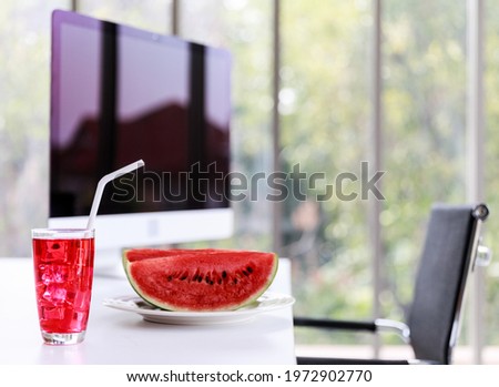 Closeup shot of iced red mixed berry juice cold iced cocktail soft drink in tall glass  and watermelon on working desk with chair big computer screen monitor
