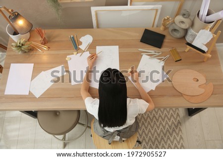 Young woman drawing male portrait at table indoors, above view