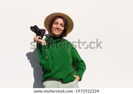 Woman in green casual sweater and hat outdoor on white wall background happy positive tourist with professional camera ready to explore summer city streets