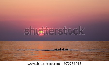 People silhouettes on rowing boat in front of sunset background. Front view