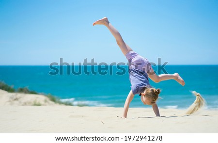 Little girl doing somersault on the beach. Outdoor games Royalty-Free Stock Photo #1972941278