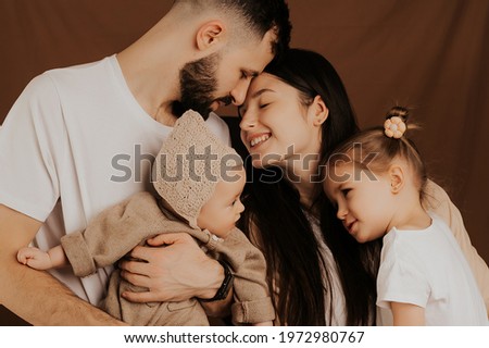 A young sincere family where a stylish bearded father and a cute wife hold their cute children in their arms. Family photo shoot in the studio